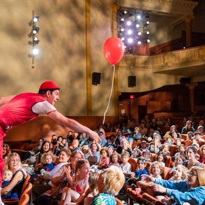 A person holds a baloon out to a group of families and children sitting inside a theater