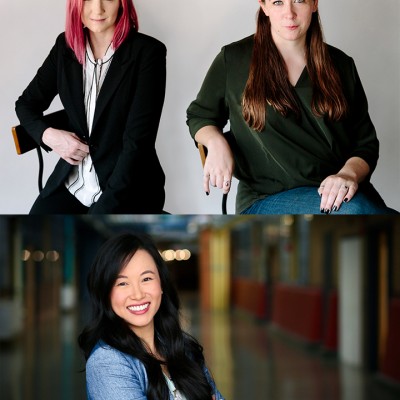 Portraits of three women. At the top, a white woman with shoulder-length straight pink hair, wearing a white button-down shirt and a black blazer, sits in a chair beside a white woman with long straight brown hair, jeans, and a dark green long-sleeved shirt. On the bottom, a smiling Asian woman with long straight black hair and a long-sleeved blue shirt stands with her arms crossed 