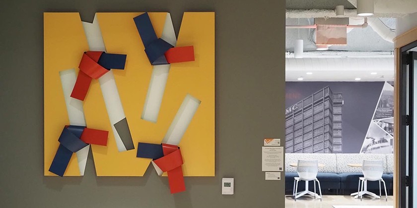 Bright yellow, red, blue, and white abstract metal art hanging on a wall inside a business office