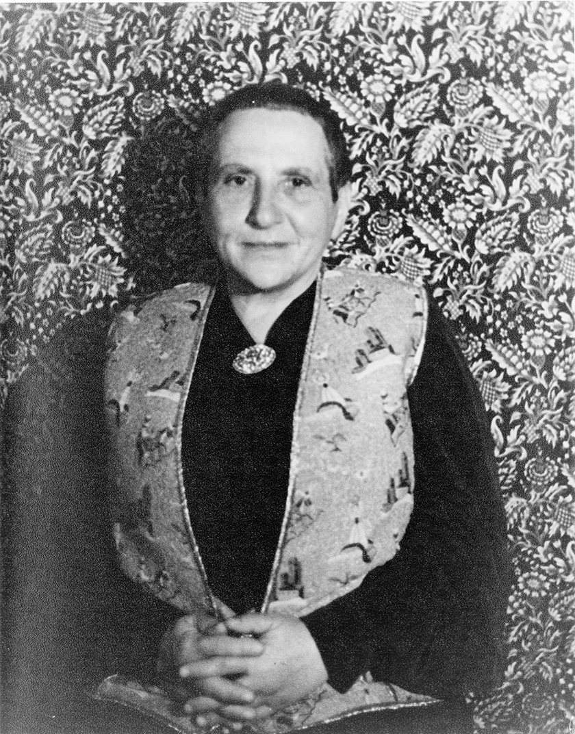 Black-and-white photo of Gertrude Stein, a woman with very short dark hair, a black long-sleeved shirt, and a patterned vest