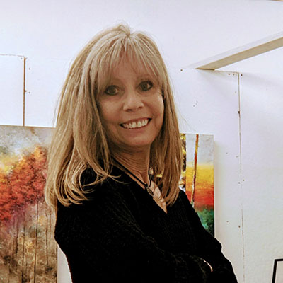 Image of artist Kathy Mazur in her studio, smiling directly at the camera