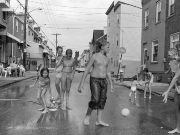 A black and white photo of a Pittsburgh city street, with dozens of children playing in water.