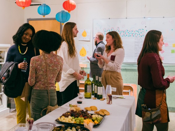 Seven people stand around a table networking with food and drinks