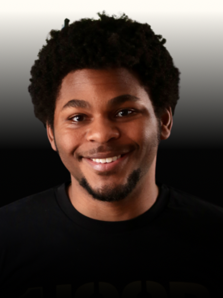 Smiling portrait of a person with short, curly dark hair and a trimmed goatee, wearing a black shirt