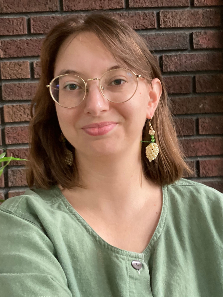 A smiling woman with shoulder-length brown hair wearing round glasses and grape-shaped earrings.