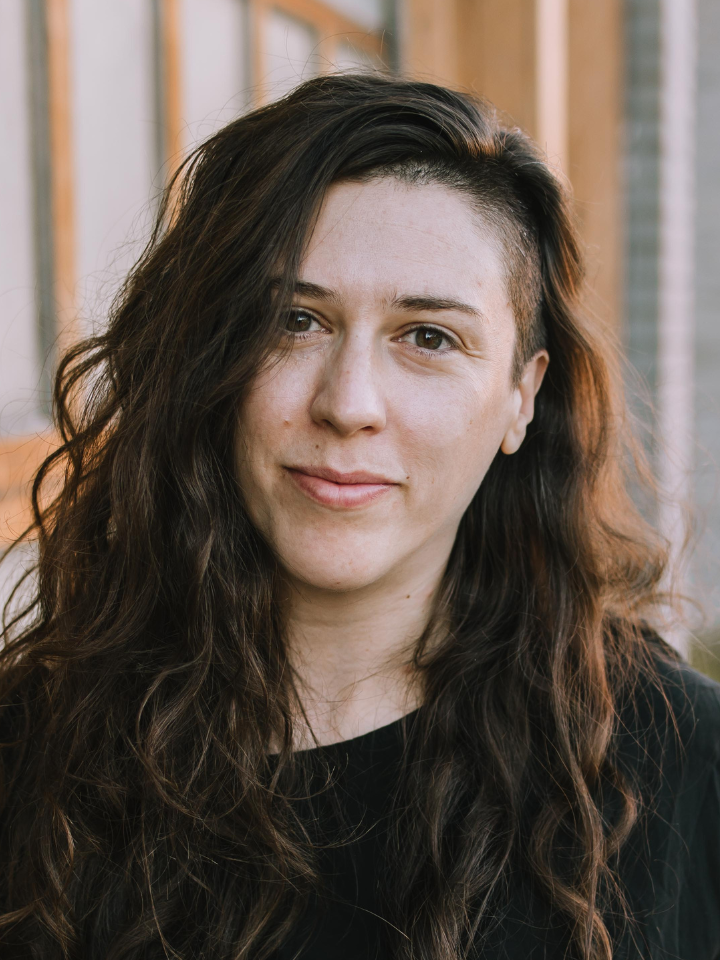 Close-up portrait of a person with long dark wavy hair, wearing a dark top