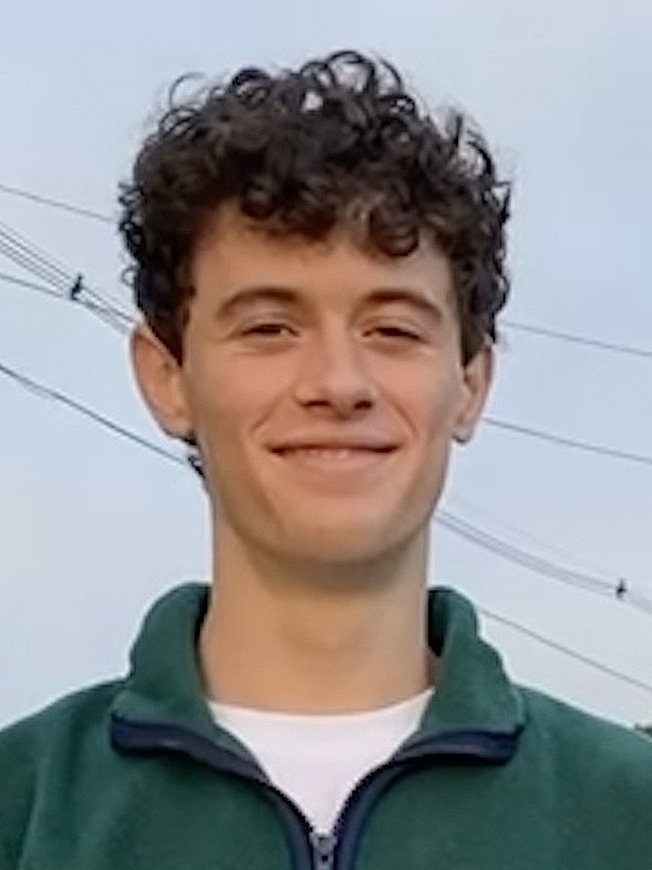 Portrait of a smiling white man with short dark curly hair, a white t-shirt, and a green zippered pullover