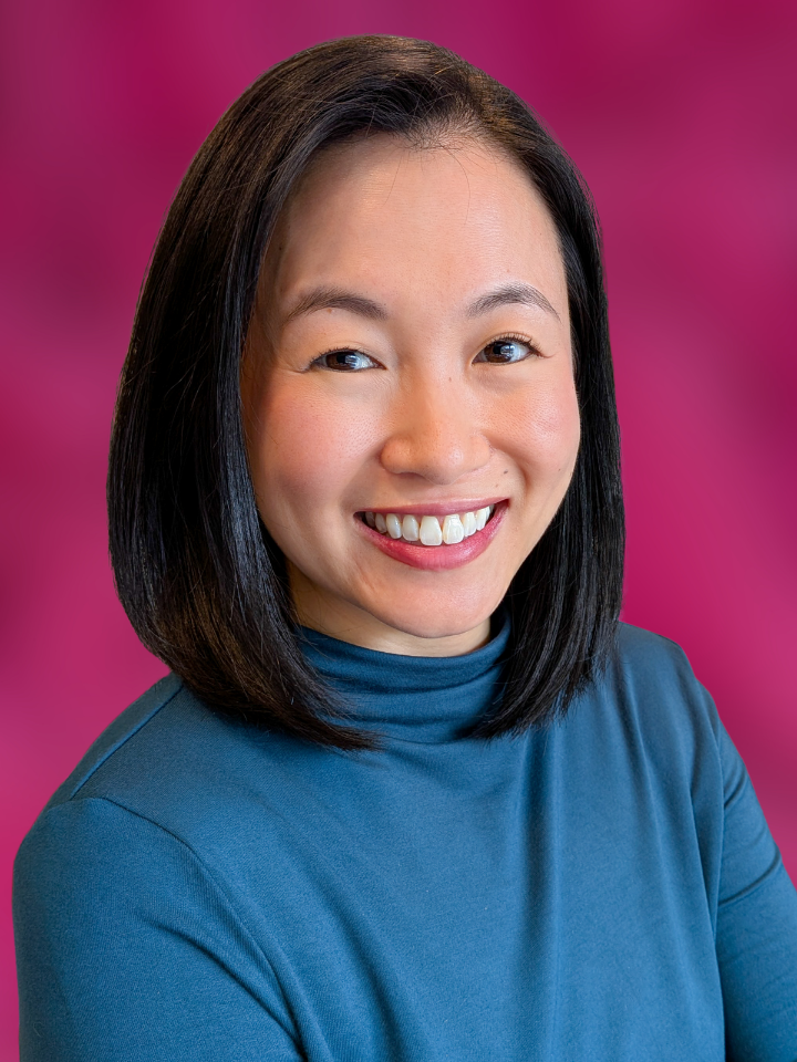 A woman with shoulder-length dark hair smiles against a pink background.