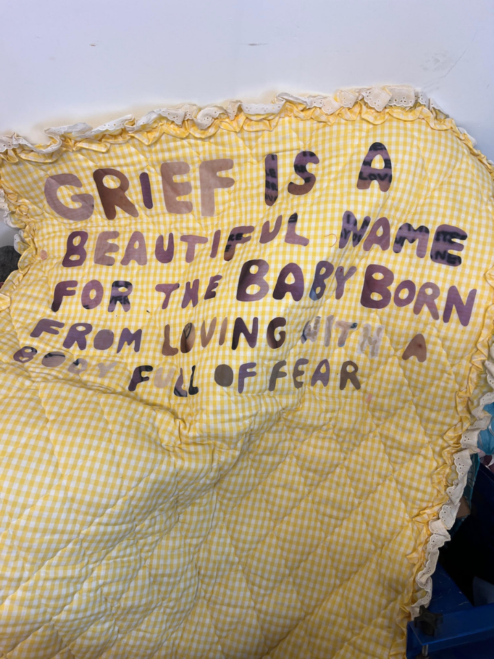 Yellow quilt with hand-sewn text about grief being a beautiful name for a baby born of fear