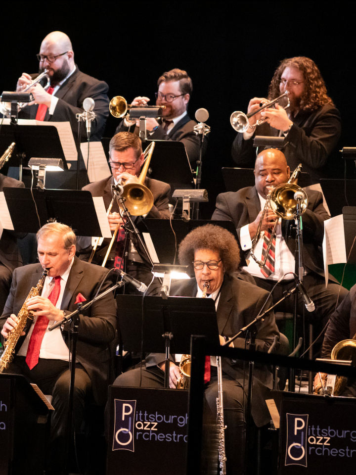 A jazz orchestra performs on stage with various brass and woodwind instruments.