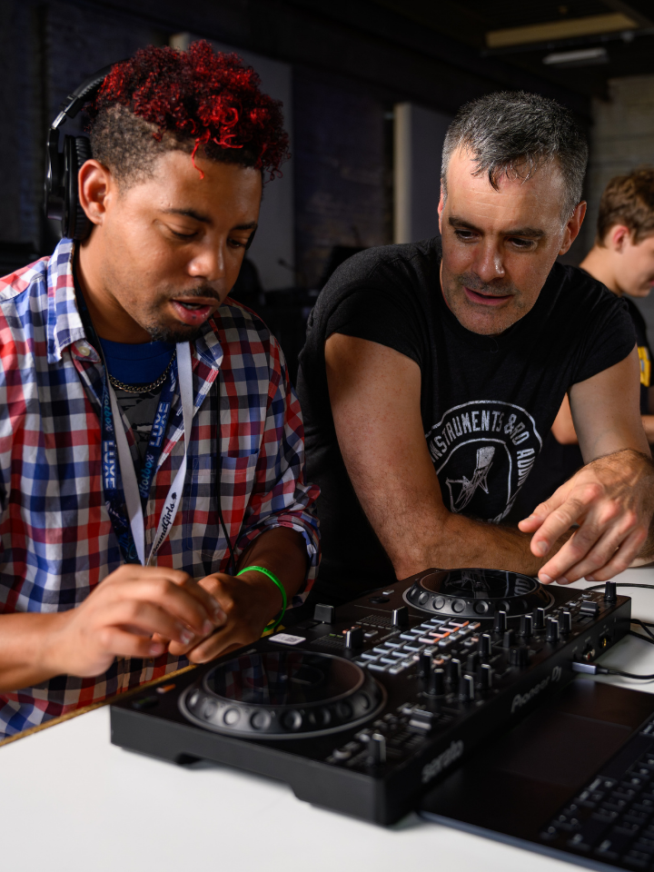Two people using DJ equipment, while two others work at laptops in the background.