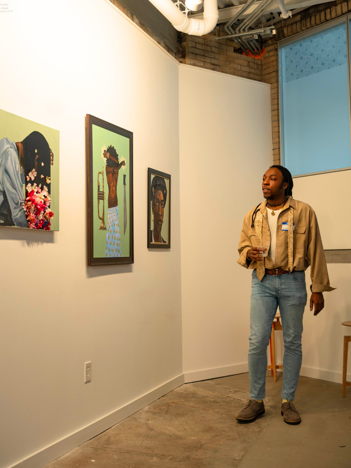 A person observes three colorful portraits hung on a white gallery wall.