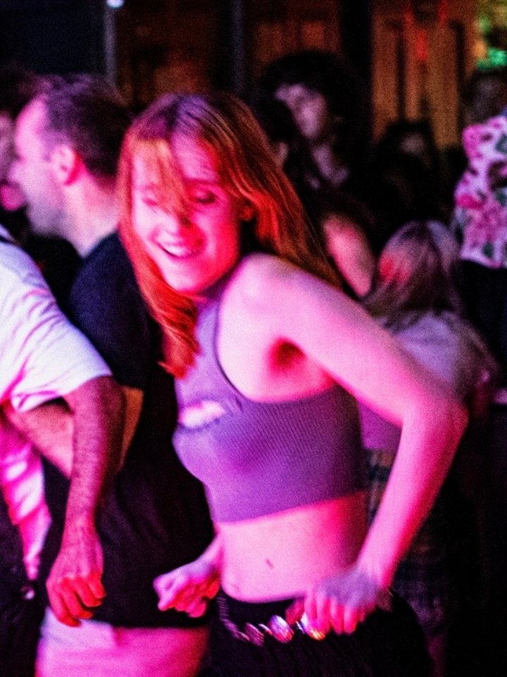 People dancing energetically in a vibrant, dimly lit venue with colorful lights all around.