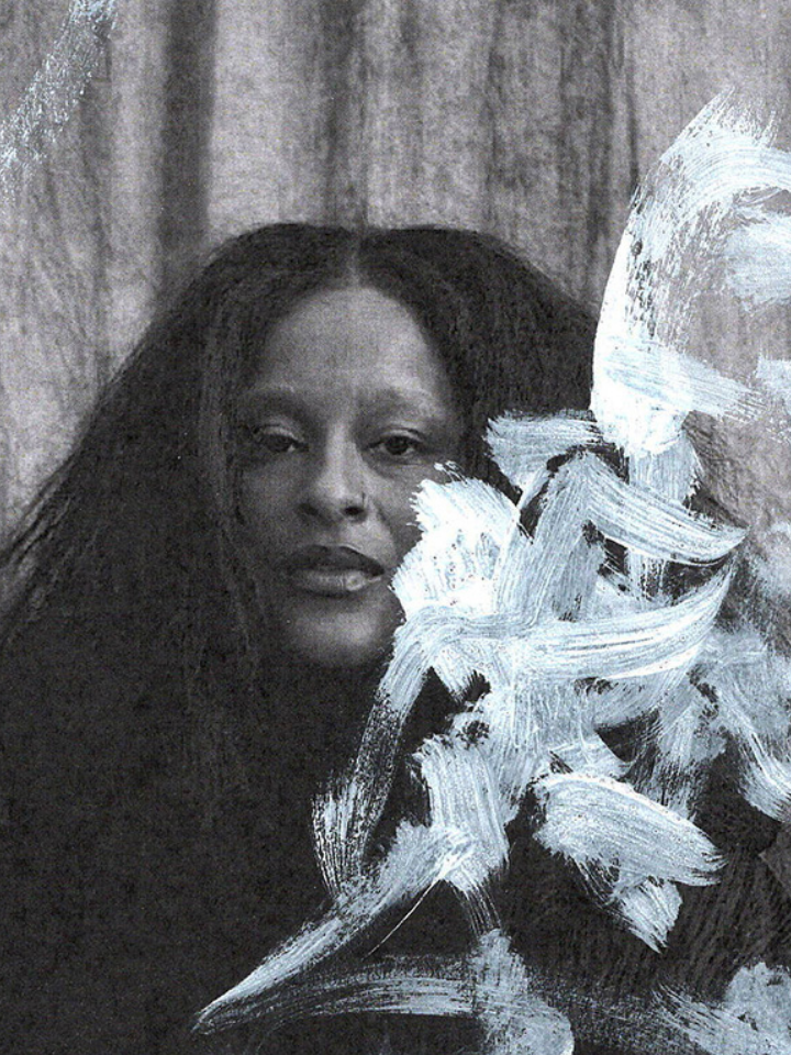 Person with long hair sits behind sheer paint strokes on a textured background.
