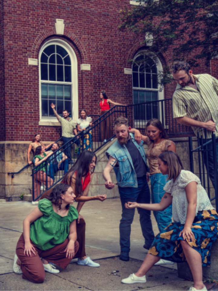 A group of people interact on a sidewalk and stairs outside a red brick building