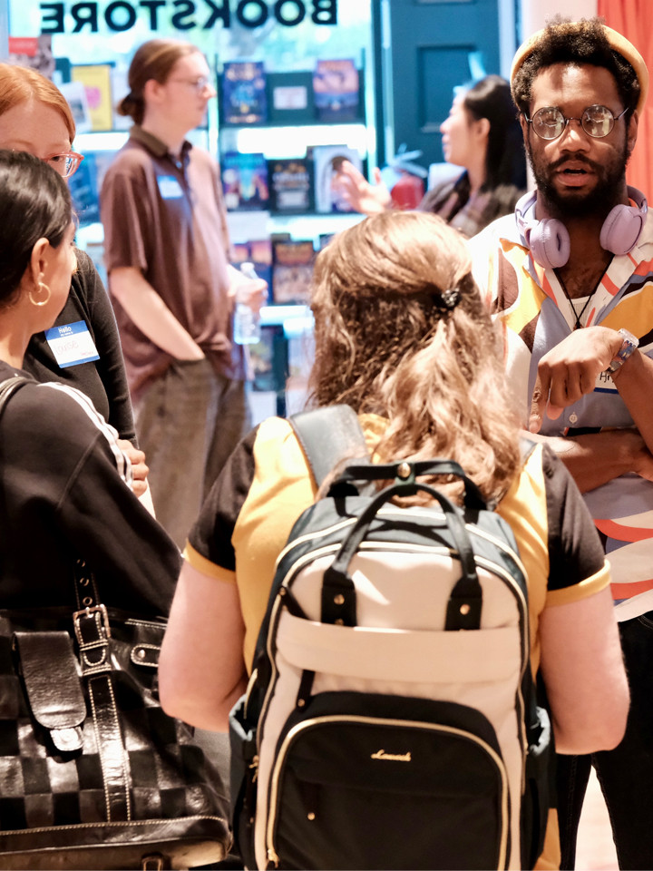 A group of people talking inside a bookstore near a display of books.