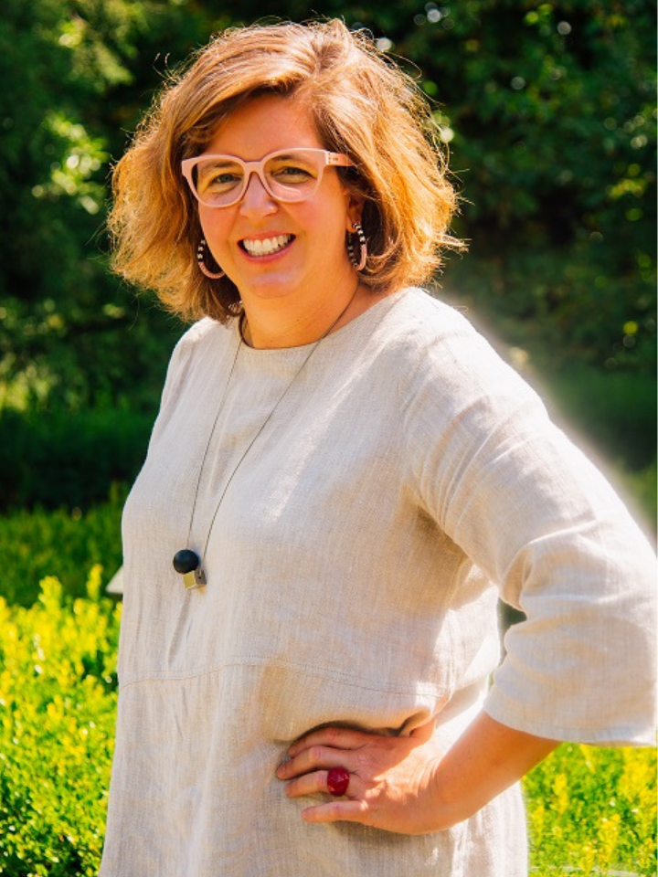 Woman with short hair and glasses smiling outdoors in sunlight