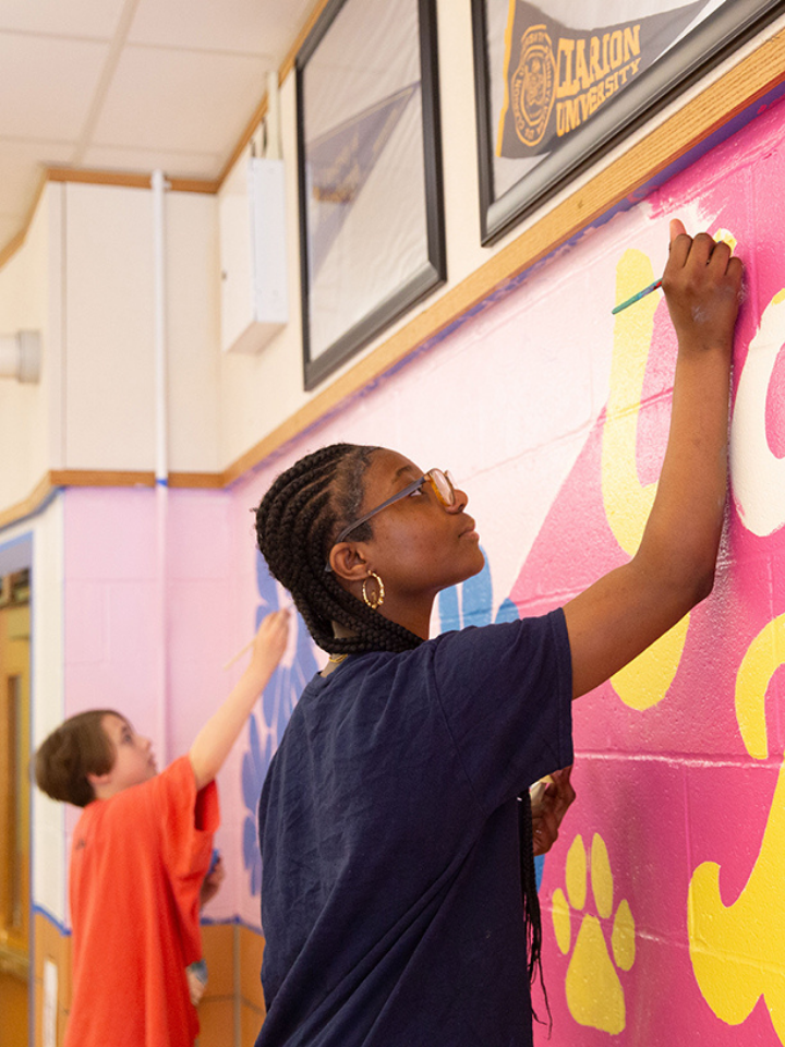 Two people painting large, colorful letters on a wall mural