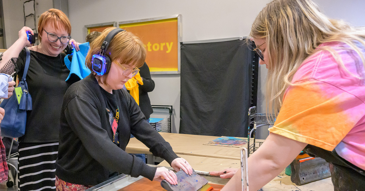 Three people work together on a screen printing project in a classroom setting.