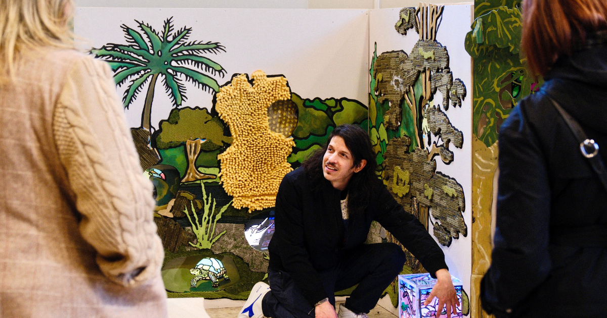 A person crouches by a colorful jungle-themed display, talking to two others