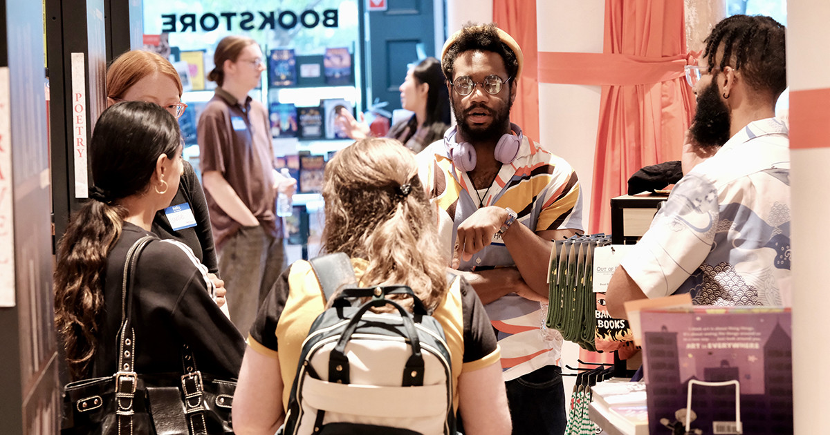 A group of people talking inside a bookstore near a display of books.