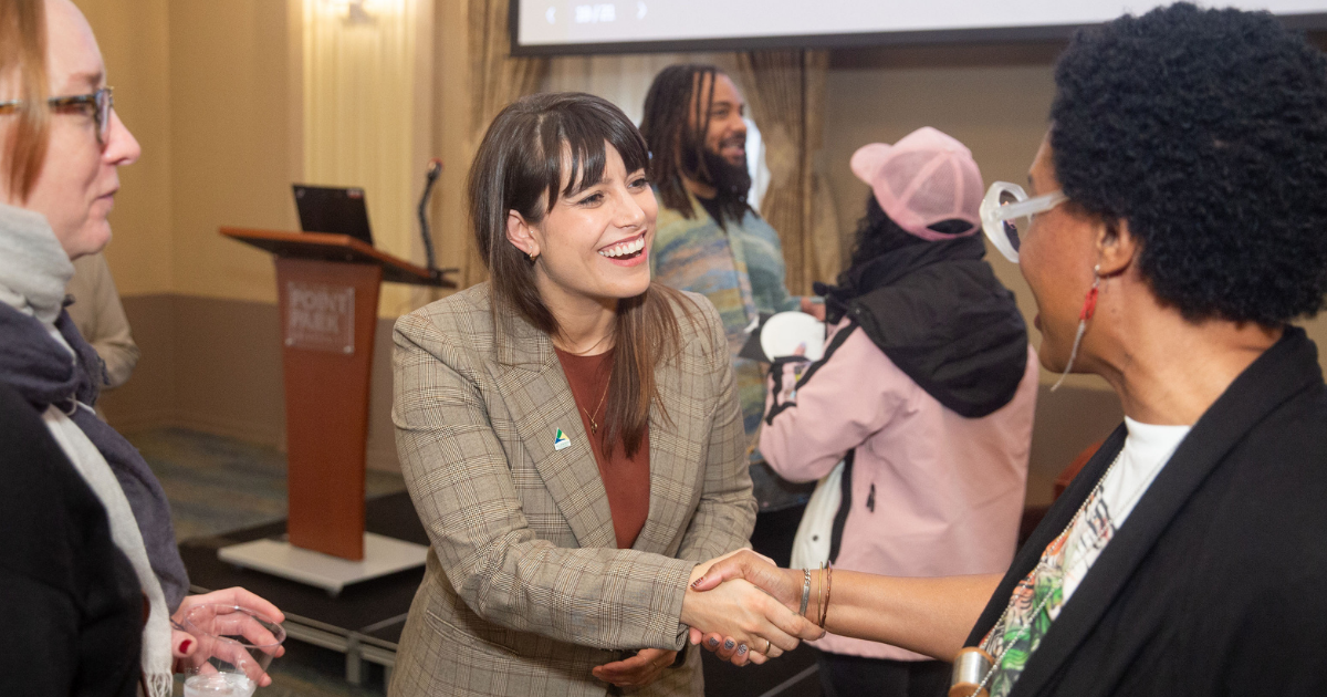 A woman in a plaid blazer smiles while talking to others at an indoor event.