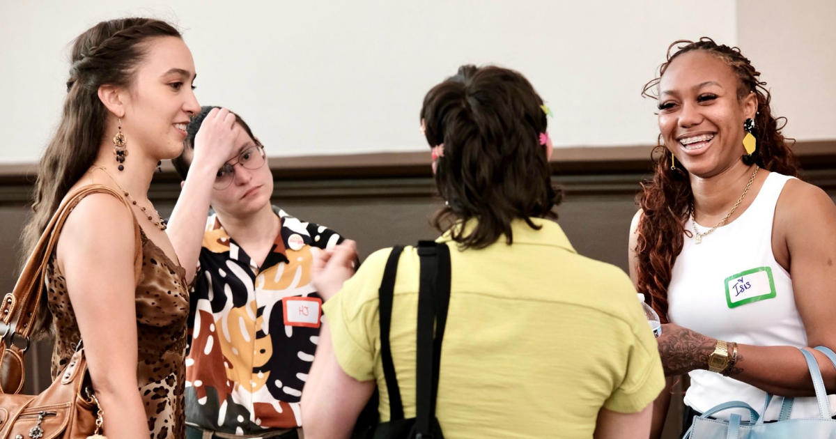 Four people stand together indoors, talking and smiling at a social event.