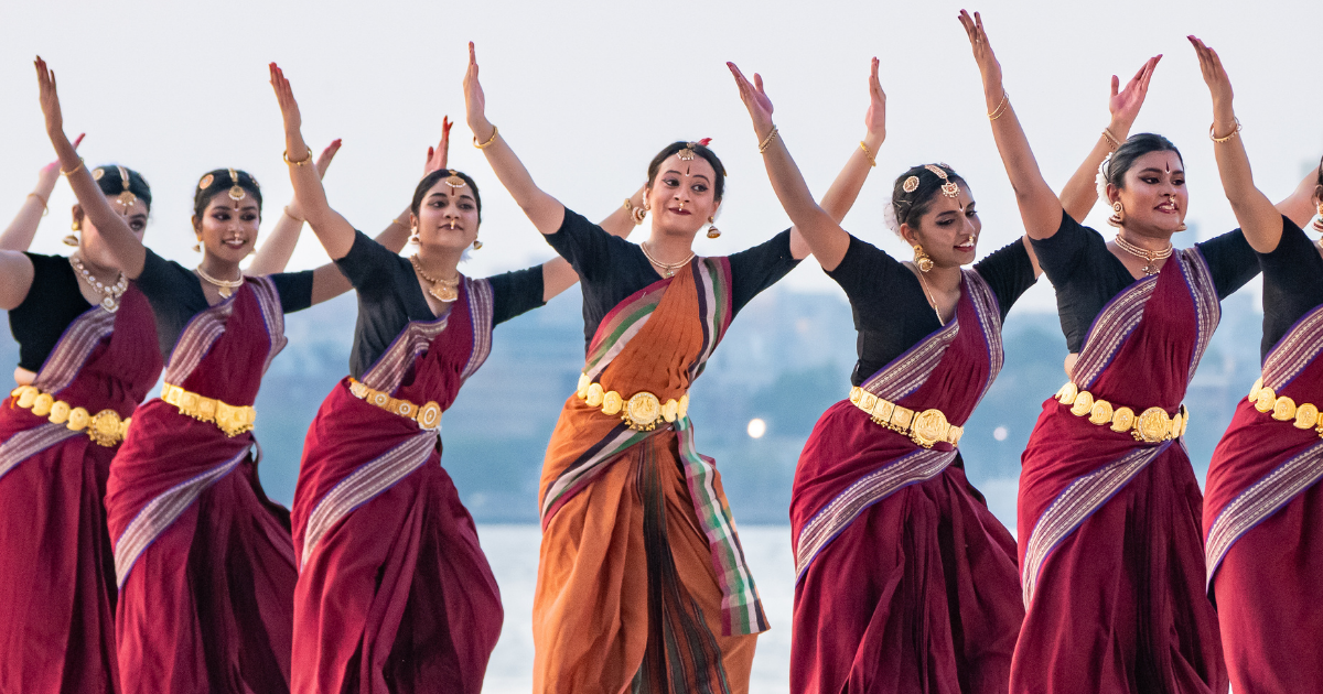Three women perform a traditional Indian dance in colorful sarees and gold jewelry.