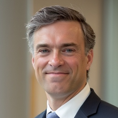 A smiling portrait of a man with short gray hair wearing a blue jacket and tie