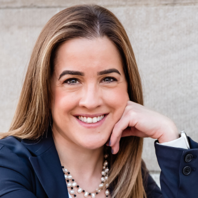 Smiling woman with long straight hair wearing a navy blazer and layered pearl necklace