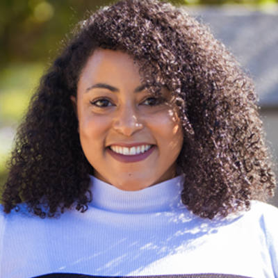 Smiling portrait of woman with shoulder length curly dark hair wearing a black-and-white shirt