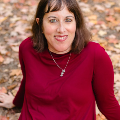 Dorit Sasson, a caucasian woman with short brown hair and bangs, smiling on an autumnal leafy background.