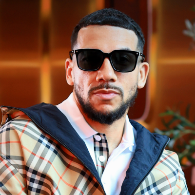 A man with a beard wearing sunglasses and a tan plaid jacket over a white collared shirt.