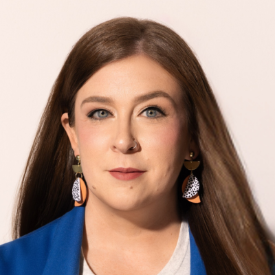 ortrait of a person with long brown hair, wearing blue outerwear over a white top, and dangling earrings
