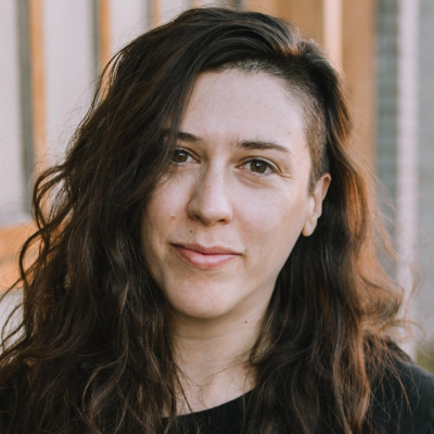 Close-up portrait of a person with long dark wavy hair, wearing a dark top