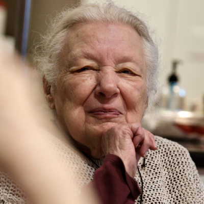 A smiling portrait of a woman with long gray hair wearing a brown and maroon sweater