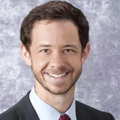 Portrait of a smiling man with short brown hair and facial hair wearing a black suite