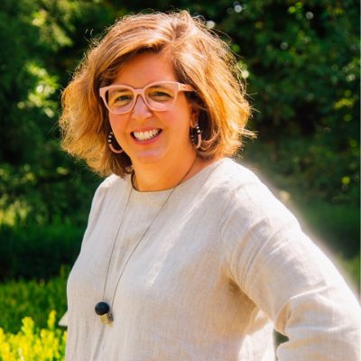Woman with short hair and glasses smiling outdoors in sunlight