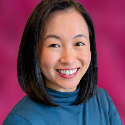 A woman with shoulder-length dark hair smiles against a pink background.
