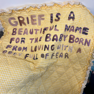 Yellow quilt with hand-sewn text about grief being a beautiful name for a baby born of fear