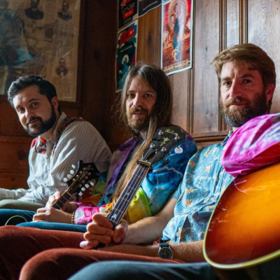 3 people sitting with string instruments in a wood-paneled room.