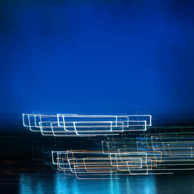 Long exposure of light trails reflected on water against a dark blue background.