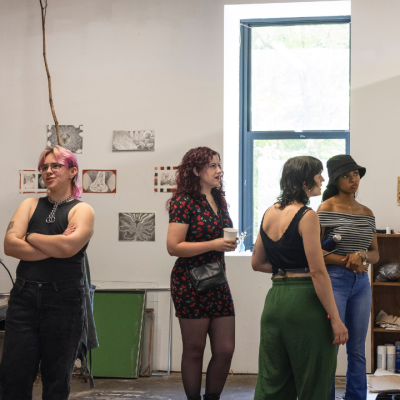 Four people stand and talk in an art studio with colorful rugs and artwork on the walls.