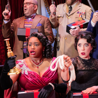 People in costumes hold various weapons and black boxes in a dramatic scene.