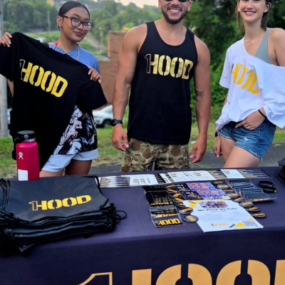 Three people stand behind a table of HOOD branded apparel and materials.