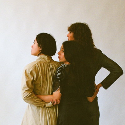 Three people in different outfits stand close together, facing away from the camera.