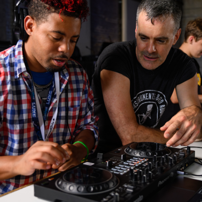 Two people using DJ equipment, while two others work at laptops in the background.
