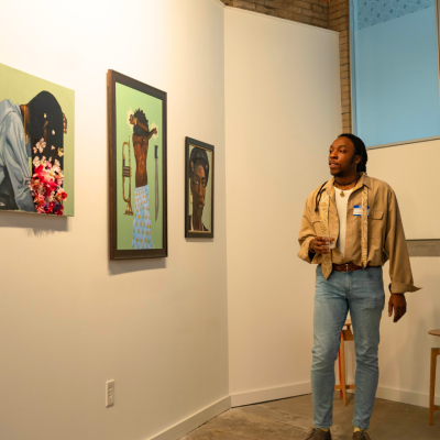 A person observes three colorful portraits hung on a white gallery wall.