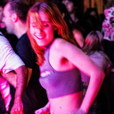 People dancing energetically in a vibrant, dimly lit venue with colorful lights all around.