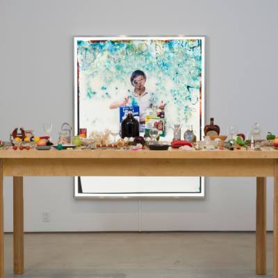 A wooden table with assorted food items, set in front of a large framed portrait on the wall.